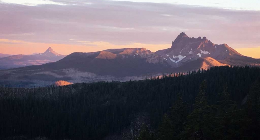 A mountainous landscape appears purple and pink while the sun is either setting or rising. 